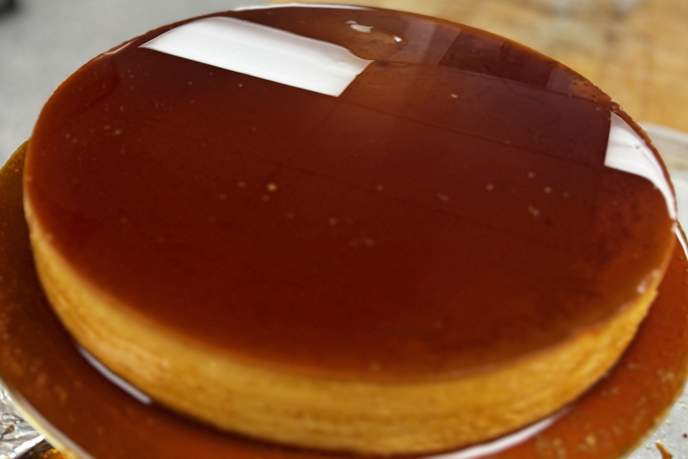Close-up of a round flan with a glossy caramel topping and caramel sauce pooled around it.