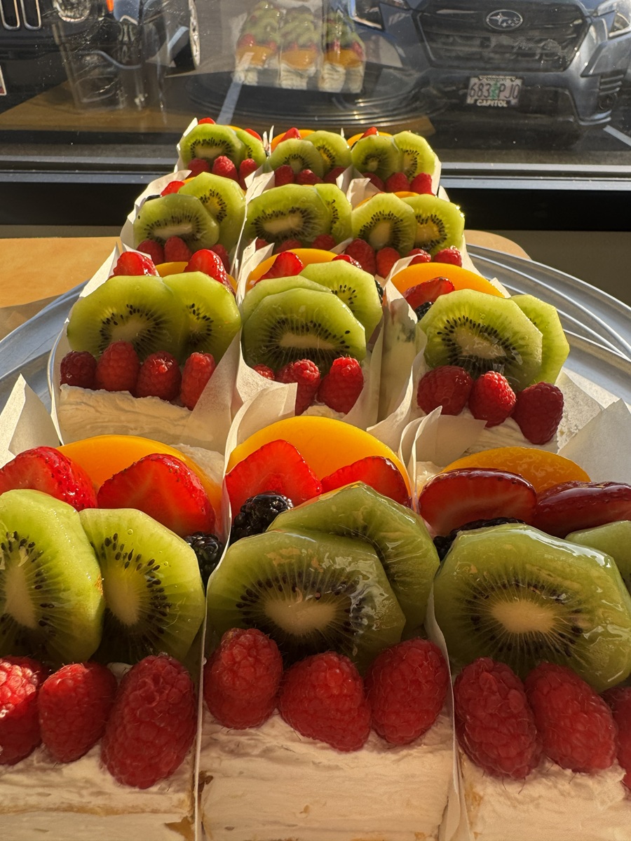 Individual mil hojas pastries with flaky puff pastry and whipped cream, topped with kiwi slices, raspberries, and other fresh fruit, arranged on a tray.