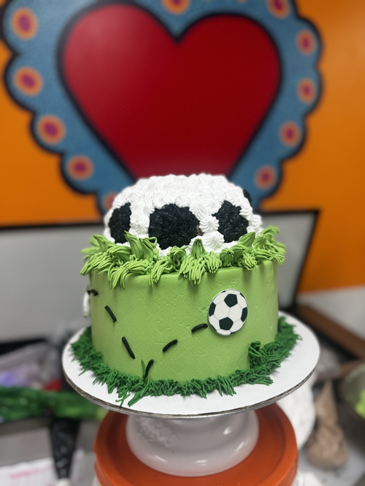 Green soccer-themed cake with grass piping, a soccer ball topper, and a small soccer ball decoration on the side.