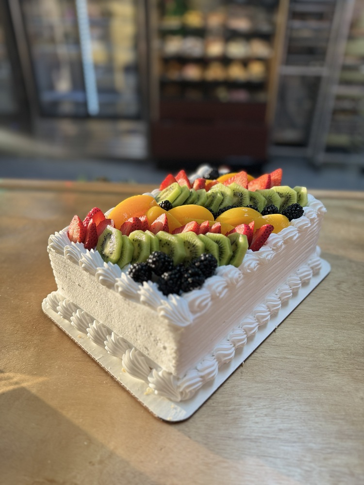 Rectangular mil hojas cake with whipped cream frosting and piped borders, topped with fresh fruit including strawberries, kiwi, blackberries, and peaches.