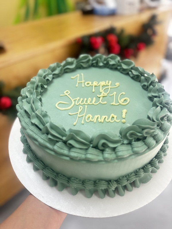 Sage green buttercream sweet sixteen cake with piped ruffle borders and “Happy Sweet 16 Hanna!” written in light yellow icing.