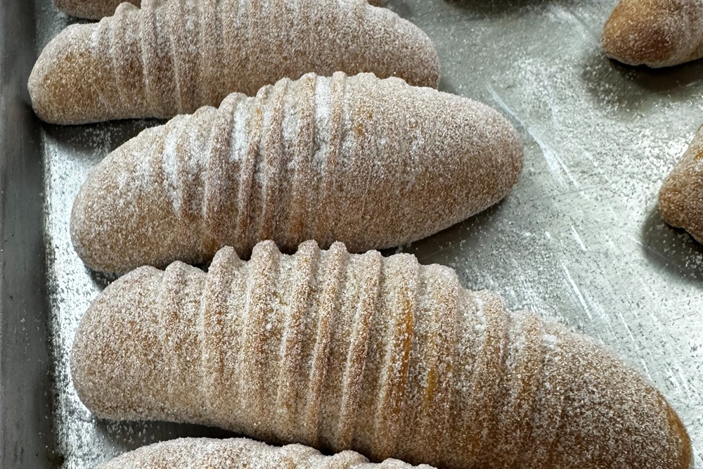 Sugar-coated Guatemalan bread shaped like ridged, oval rolls arranged on a baking tray, freshly baked and dusted with sugar.